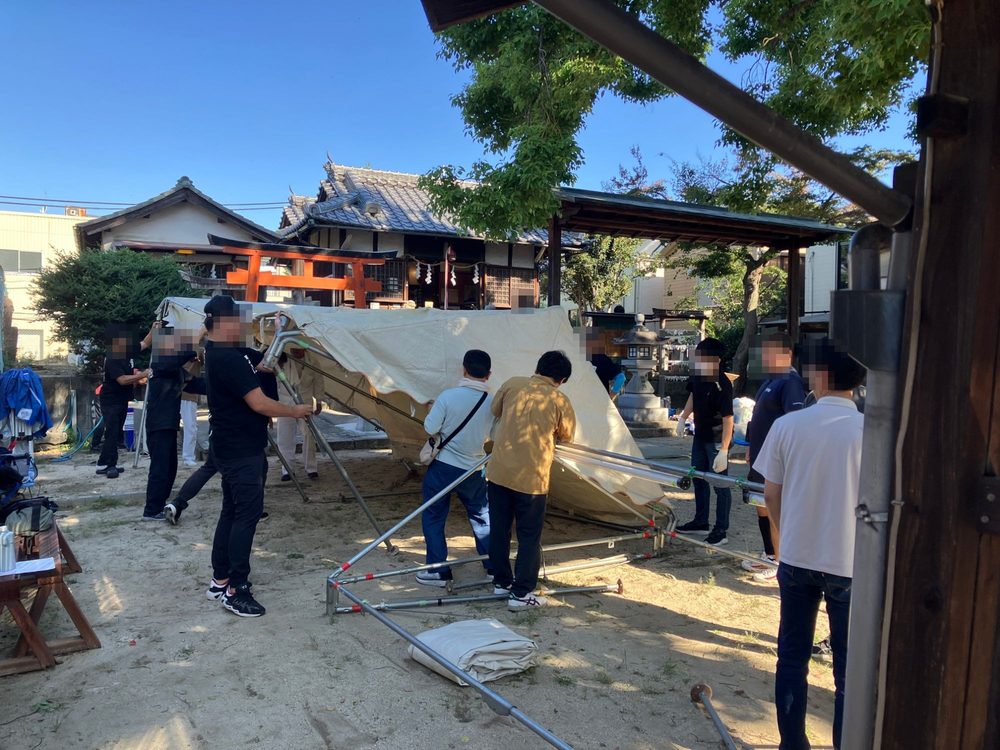 神社の境内で、大勢でテントを組み立てているところ